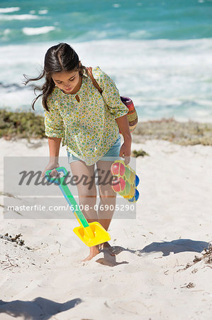 Girl carrying shovel and toy on the beach