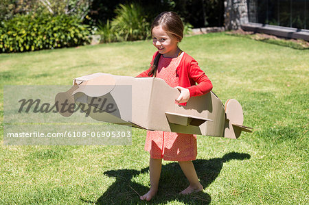 Girl playing with a cardboard airplane in lawn