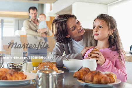 Girl having breakfast beside her mother at a kitchen counter