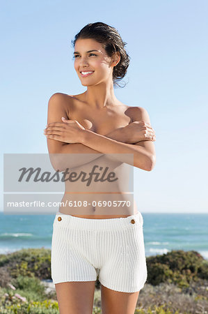 Topless woman covering her breasts with hands on the beach