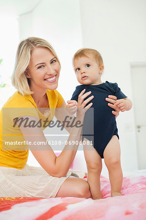 Smiling woman playing with her baby on the bed