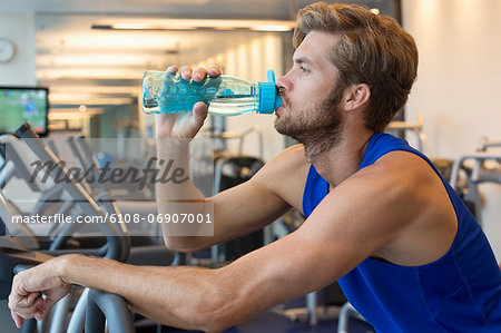 Man drinking water from a bottle at a gym - Stock Photo - Masterfile