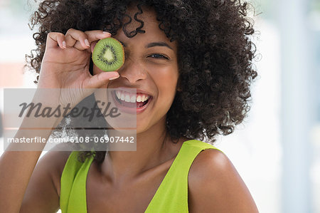 Smiling woman holding a kiwi fruit in front of her eye