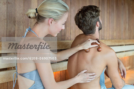 Woman massaging on her friend's back with a massager in a sauna