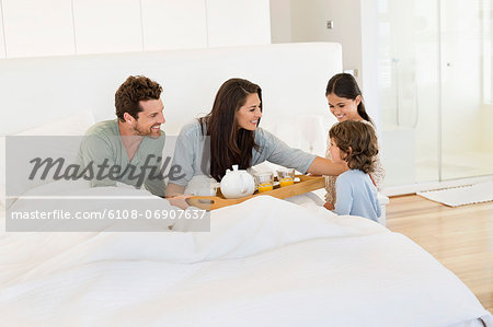 Children serving tea to their parents on the bed