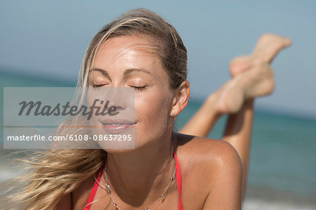 Close-up of smiling blond close eyes woman lying on the sand