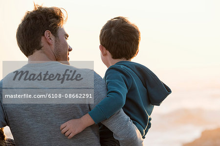 Happy father and son standing on the beach at sunset