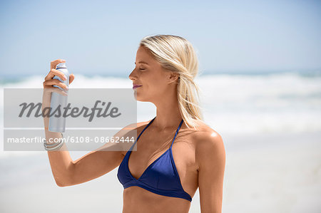 Happy woman spraying sunscreen on her face