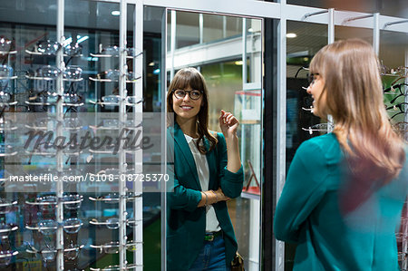 Young woman trying on eyeglasses in front of mirror in optical shop