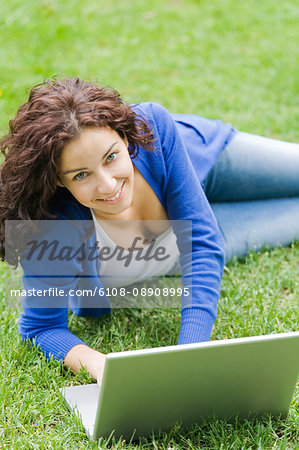 Content woman with laptop lying down in the park