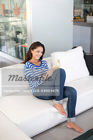 A Brunette Woman is Smiling, Relaxing on a Sofa Stock Image