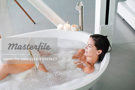 Young pretty brunette woman enjoying a bath and reading a book