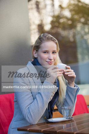 Pretty blonde woman enjoying a cup of coffee in a Cafe and smiling at camera