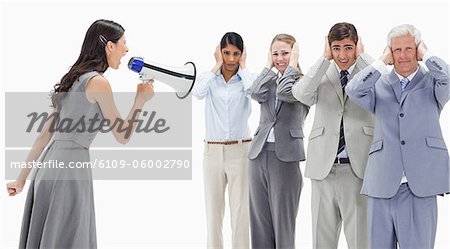 Woman yelling in a megaphone at business people with their hands over their ears against white background