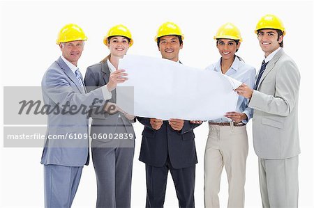 Smiling business people wearing safety helmets holding a map against white background