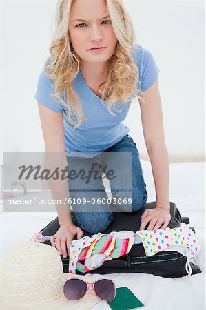 A woman looking offput that her suitcase full of clothing will ot close for her on the bed.