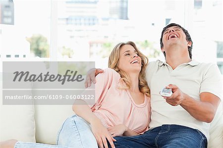 A man and woman on the couch together laughing at a funny television programme.