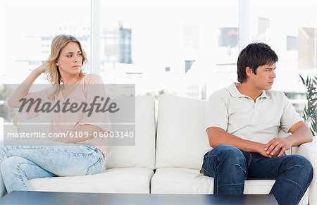 A man looking angry turned the opposite way to the woman at the other end of the couch looking upset.