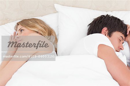 A man and woman with their backs to each other in bed, possibly after a arguement.