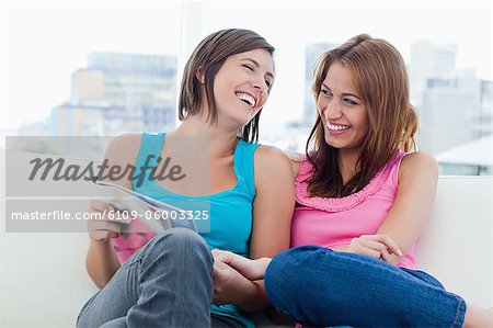 Young women laughing while looking at a review and sitting on a white sofa