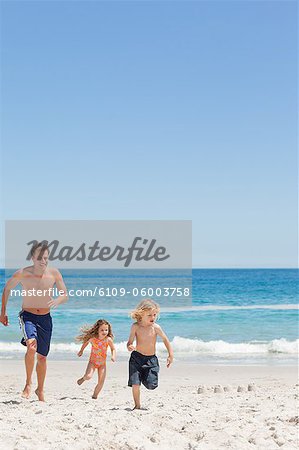 Young father running with his little children on the beach