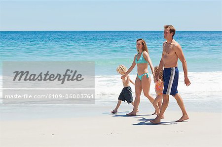 Side view of young family walking together along the beach