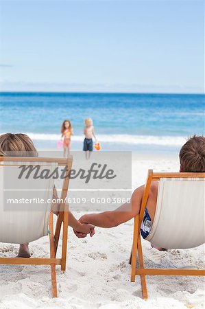 Parents holding hands while watching their little children at the beach