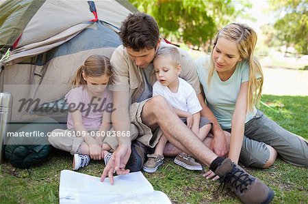 Kids look at a map that their father uses to show them where they are in the park