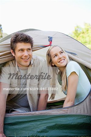 A smiling couple are almost fully in the tent as they look up to the sky