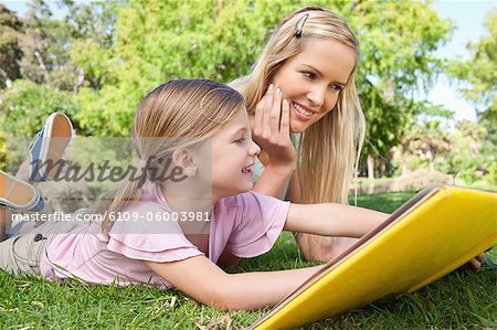 Mother and daughter reading a book together on the lawn