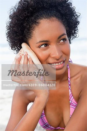 Young woman attentively listening to the sound of the sea in a shell