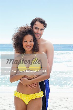 Man wearing a swimsuit smiling while he wraps his arms around his friends waist