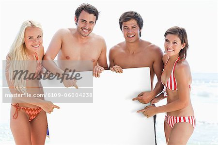 Two men and two women smiling and pointing at a large blank poster which they hold between them