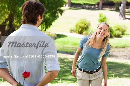 Young man in the park hiding a rose from his girlfriend