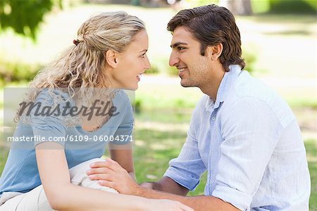Side view of a smiling young couple sitting on the grass