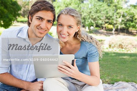 Smiling young couple with a tablet computer sitting in the park