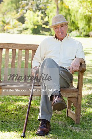 Man wearing hat while smiling as he sits on a bench and holds his cane