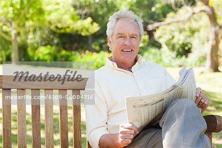 Man reading a newspaper while sitting on a wooden bench in a park