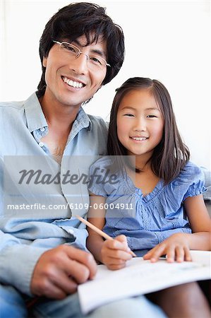 A father and daughter study together while smiling and sitting on the couch