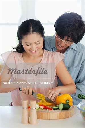 A wife chops some yellow pepper as the husband watches and smiles while in the kitchen