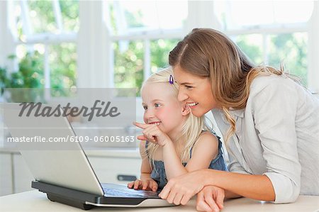 The young girl with her mother points to the laptop while they sit in the living room