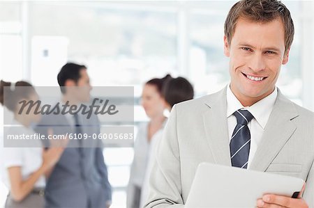 Smiling young salesman with his tablet computer and colleagues behind him