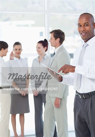 Smiling young salesman with his tablet pc and colleagues behind him