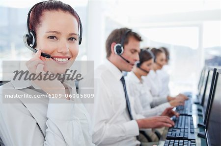 Smiling young call center agent with her colleagues behind her