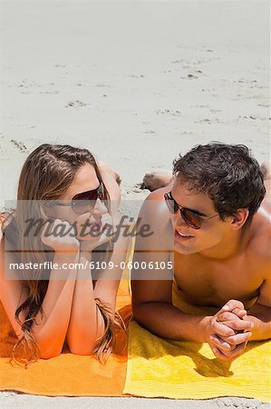 Close-up of a couple being tanning on the beach while lying on yellow towels