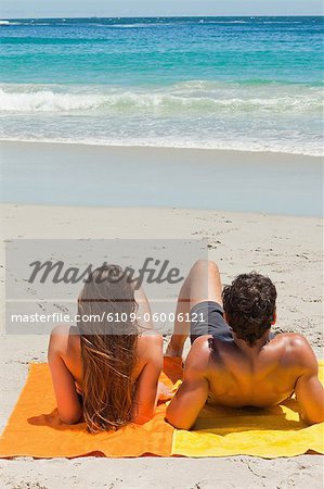 Tanned young couple lying on the beach while looking the sea