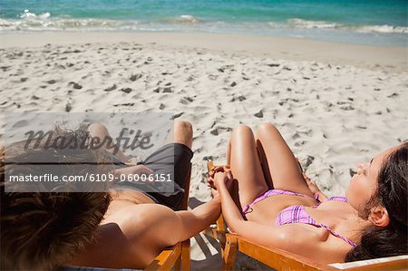 Rear view of a duo in swimsuit taking a sunbath on deck chairs in front of the ocean