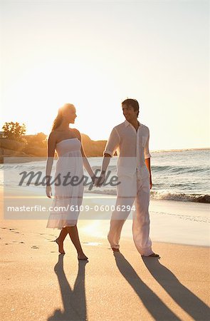 Young couple walking on the beach at sunset while holding their hands