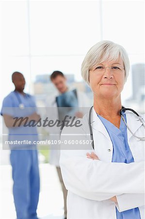 Confident doctor with arms folded and two colleagues behind her