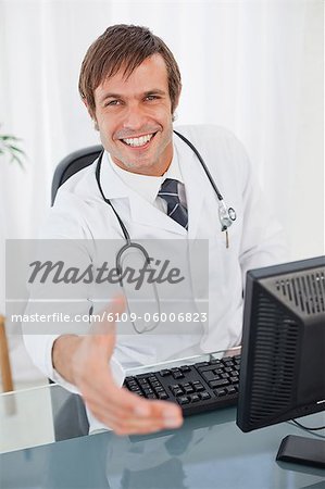 Surgeon offering a handshake while looking at the camera and sitting at a desk